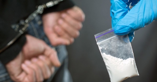 person in handcuffs, police officer holds drugs